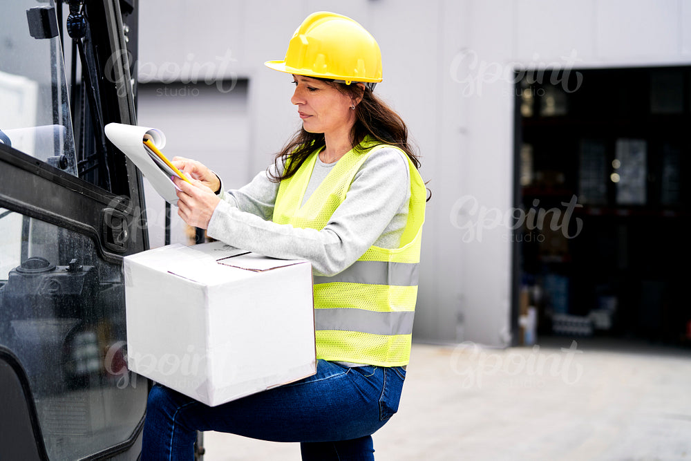 Caucasian mature woman in front of warehouse looking on documents