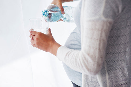 Unrecognizable pregnant woman pouring a glass of water