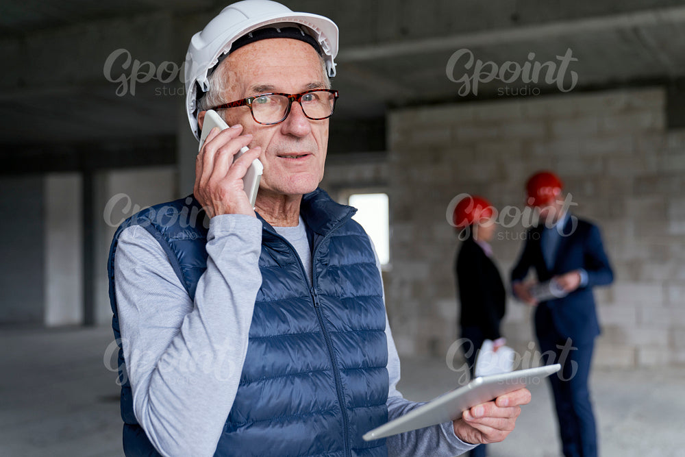 Senior investor man standing in front and discussing by mobile phone on construction site 