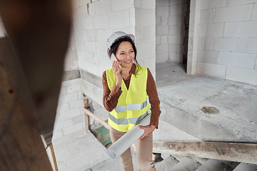 Female mature caucasian engineer standing on the stairs on construction site and talking on mobile phone