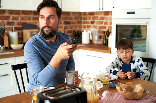 Father and son at breakfast using a mobile phone