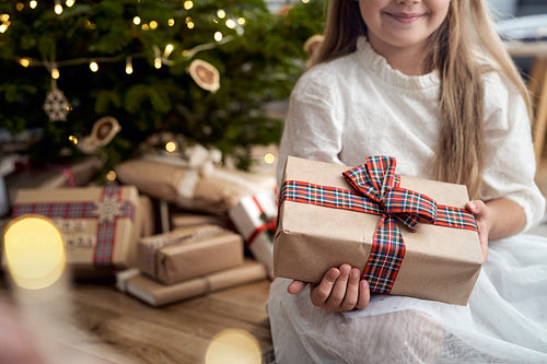 Portrait of caucasian girl and holding Christmas gift while sitting next to Christmas tree