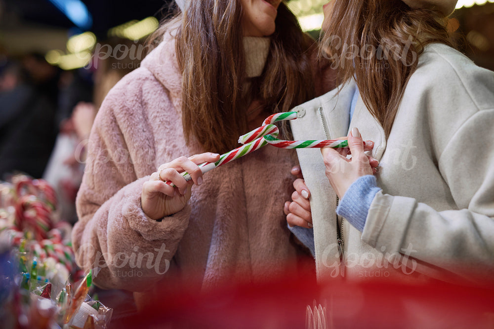 Two women buying  candy cane on Christmas market