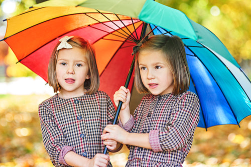 Twins girls looking for shelter with umbrella