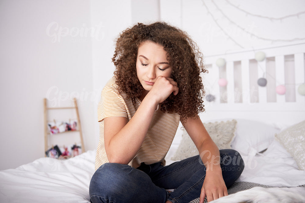 Crying teenage girl sitting on the bed in her room