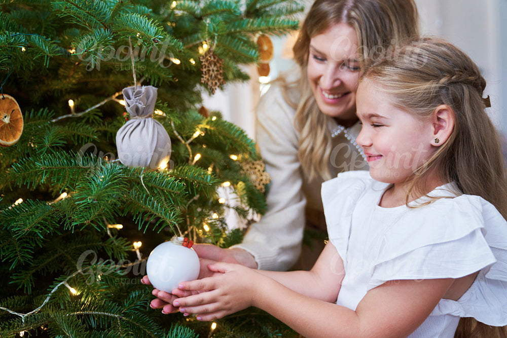 Cute girl decorating the Christmas tree with mum 