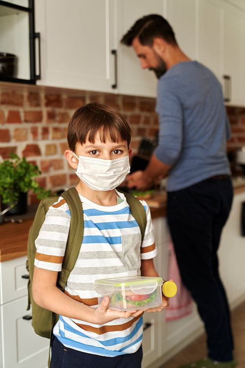 Portrait of schoolboy in protective face mask holding lunch box