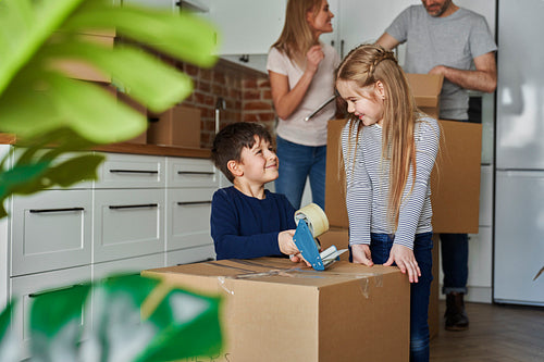 Happy siblings help with packing cardboard boxes for moving house