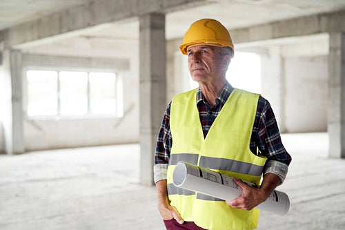 Caucasian senior engineer holding plans and standing on construction site