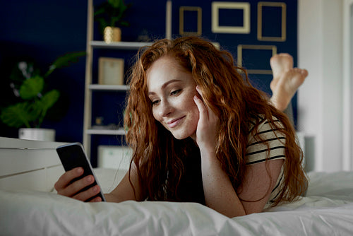 Young woman using phone while bedding