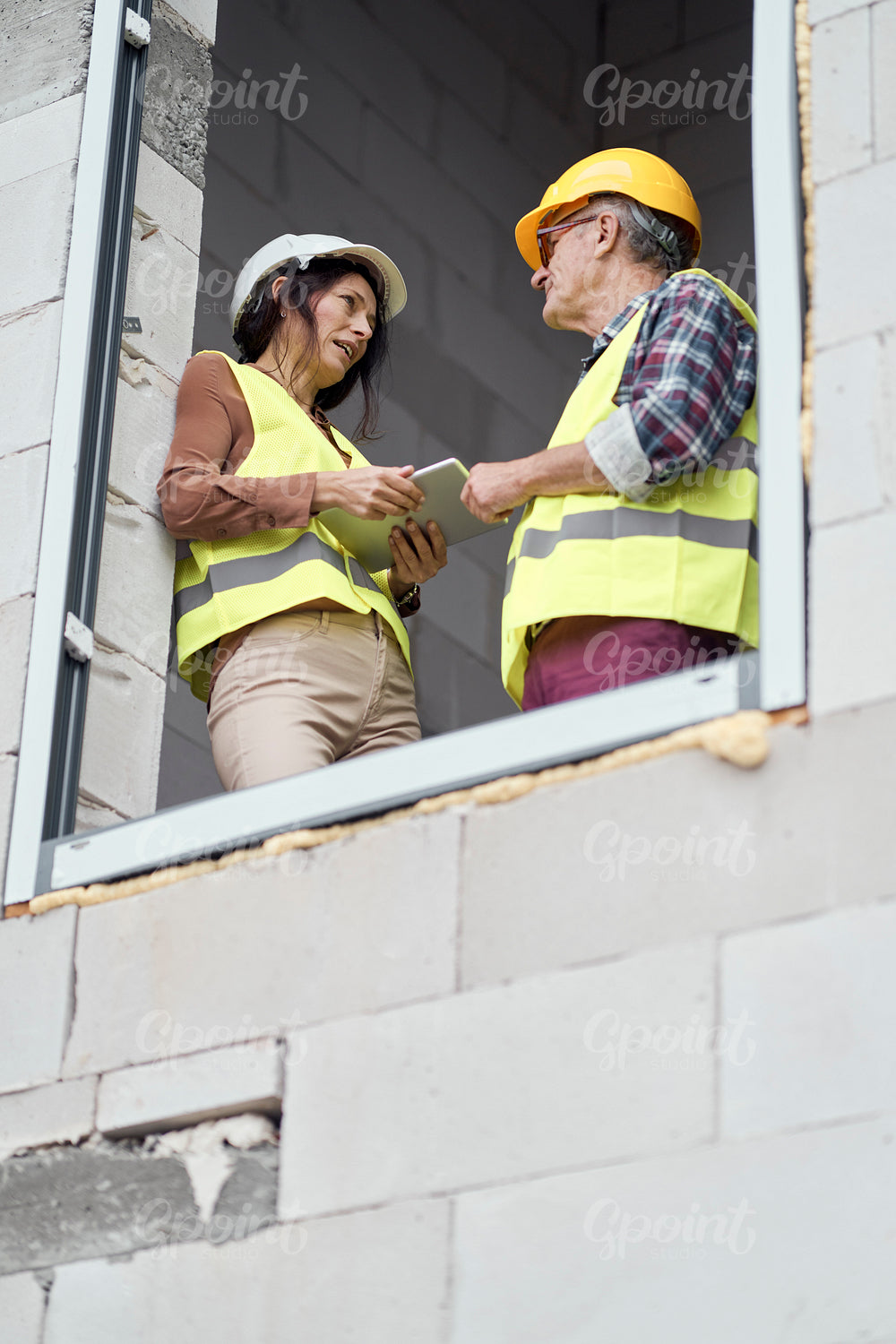 Two caucasian engineers standing near to window and discussing over digital tablet on the construction site