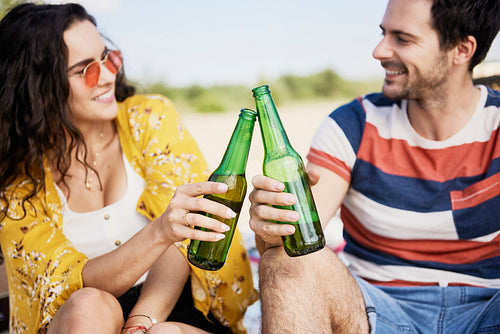 Young couple doing celebratory toast with beer bottles on beach