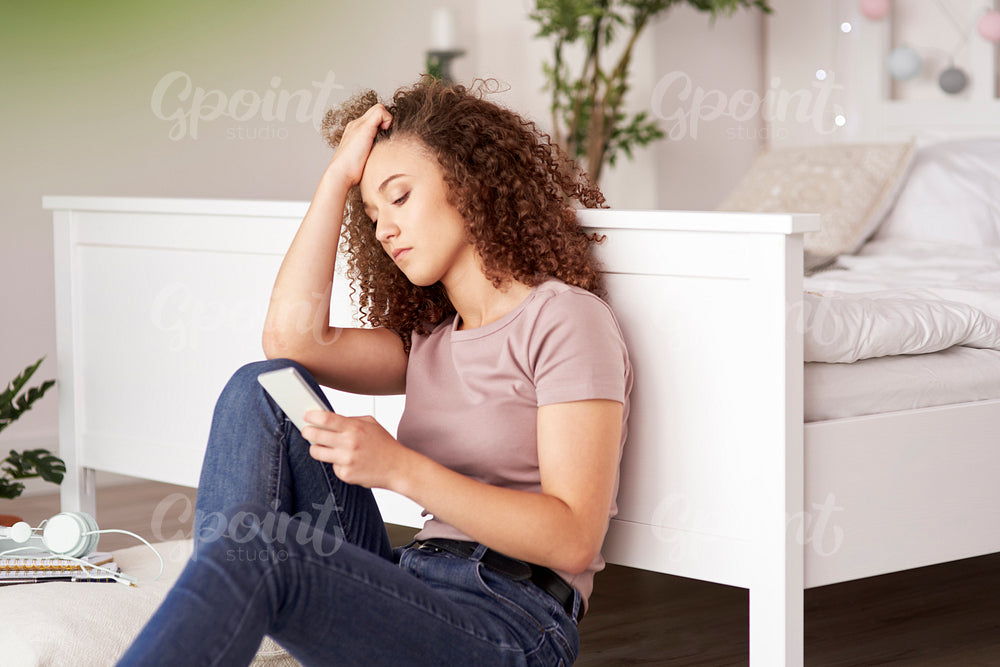 Worried teenage girl using mobile phone in her room
