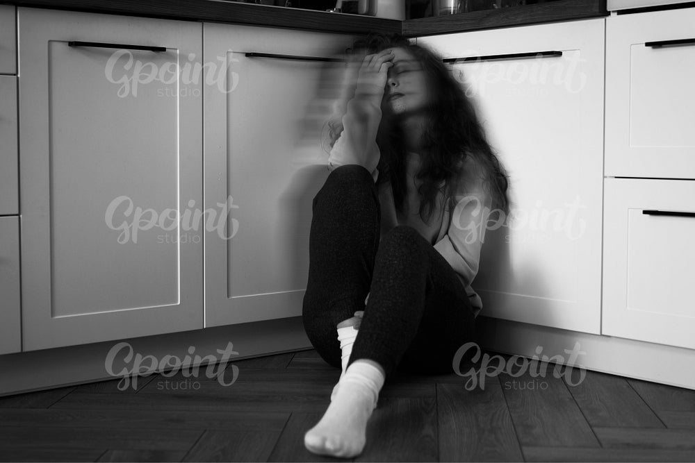 Black and white image of thoughtful young caucasian woman sitting on floor in the kitchen