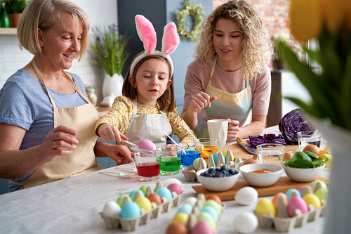 Little girl with mother and grandmother dyeing Easter eggs