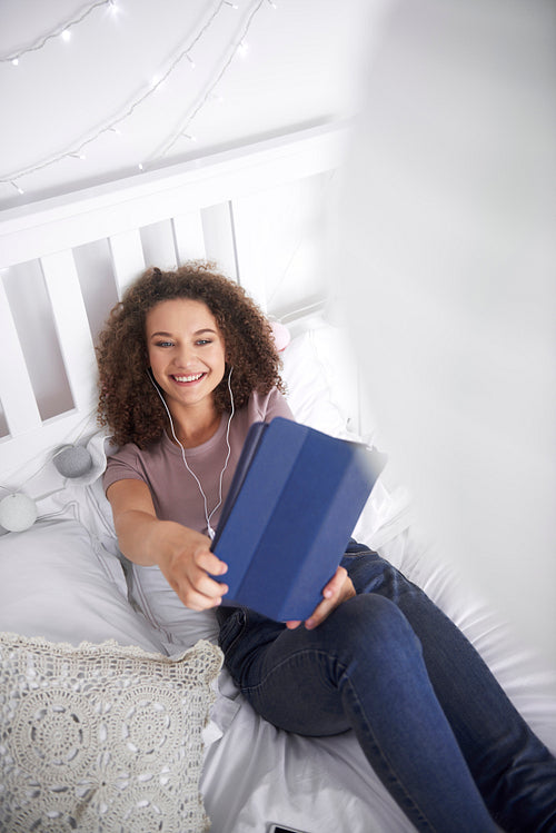 Smiling teenage girl making a selfie in her bed