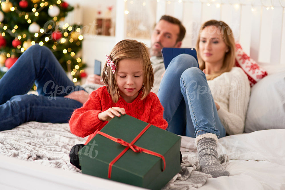 Child opening  gift and parents with technology in the background