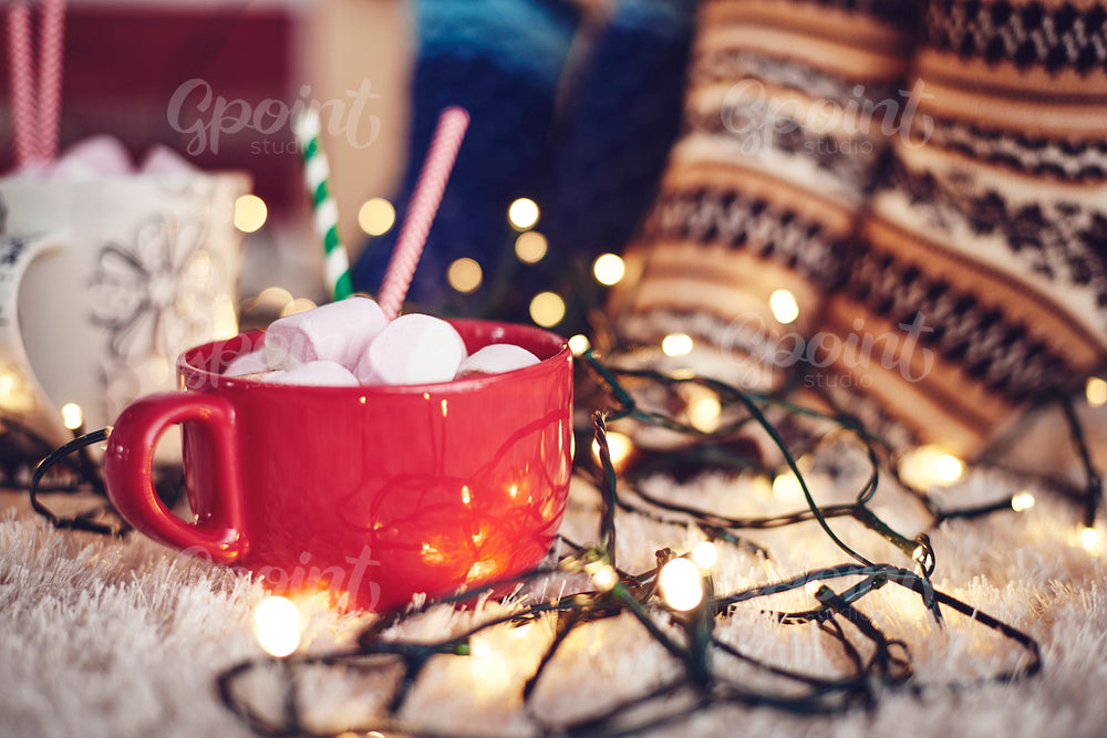 Christmas lights and mug of chocolate with marshmallow on rug