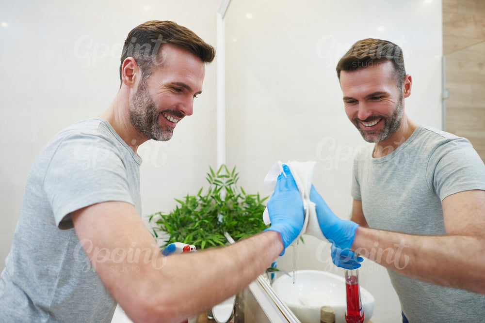 Side view of man cleaning big mirror in the bathroom