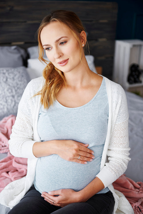 Portrait of worried pregnant woman sitting on bed