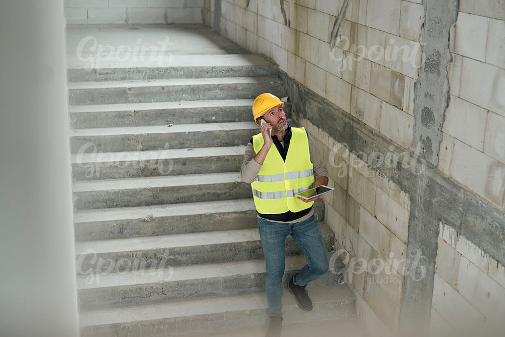 Caucasian engineer walking on stairs and browsing digital tablet on construction site