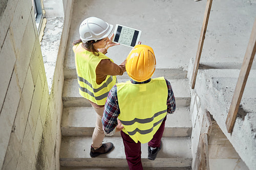 Two caucasian engineers standing on stairs and discussing over digital tablet on the construction site