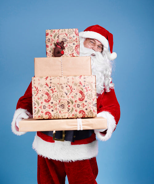 Portrait of santa claus holding stack of christmas presents