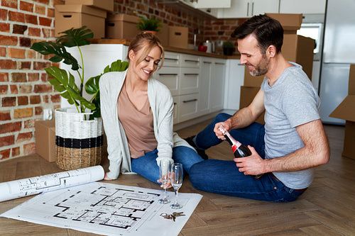 Young couple in new flat celebrating and holding ground plan