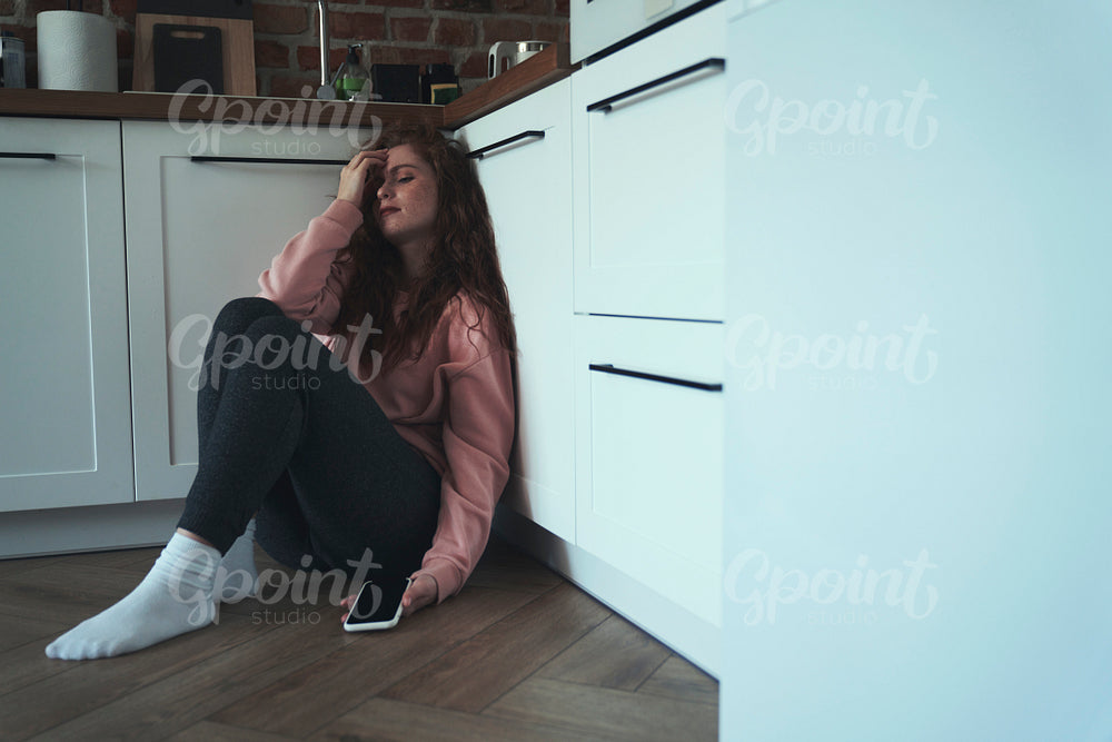 Anxious young caucasian woman sitting on floor holding mobile phone