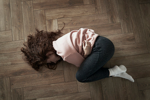 Top view of young caucasian woman lying on floor and having strong stomachache