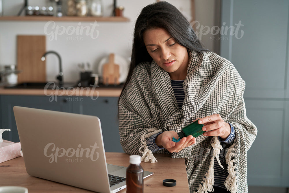 Sick woman taking medication at home in front of laptop