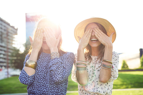 Two happy young woman covering their eyes with their hands