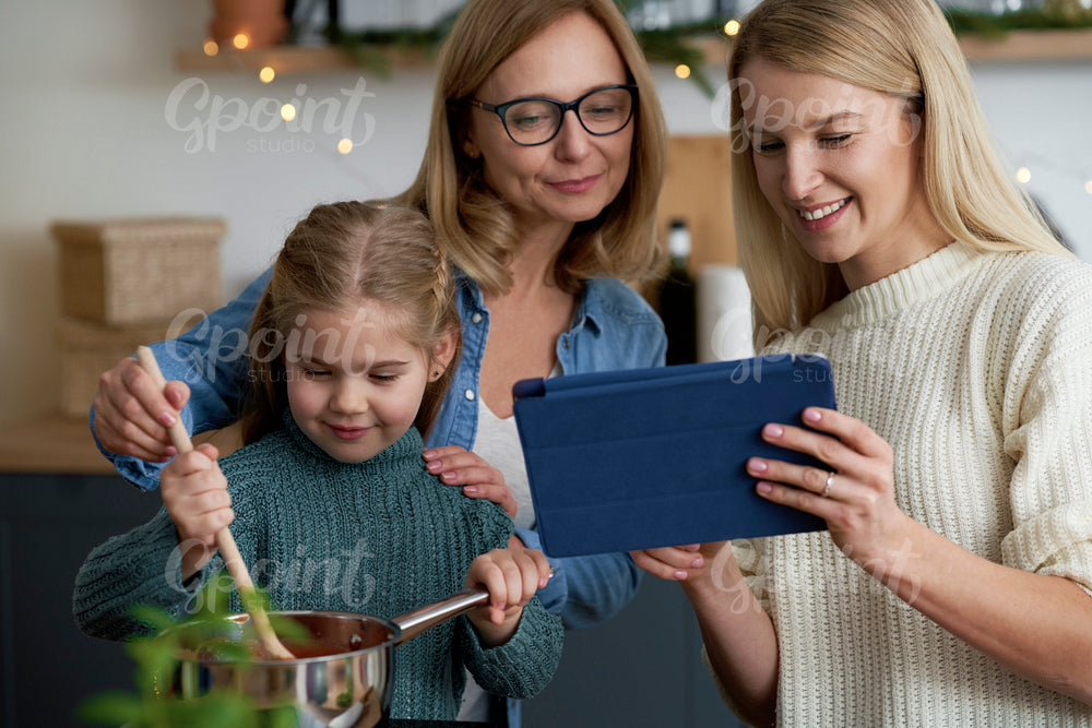 Three generations of women in the kitchen cooking with a tablet