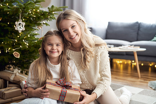 Portrait of caucasian girl and mother embracing each other and holding Christmas gift