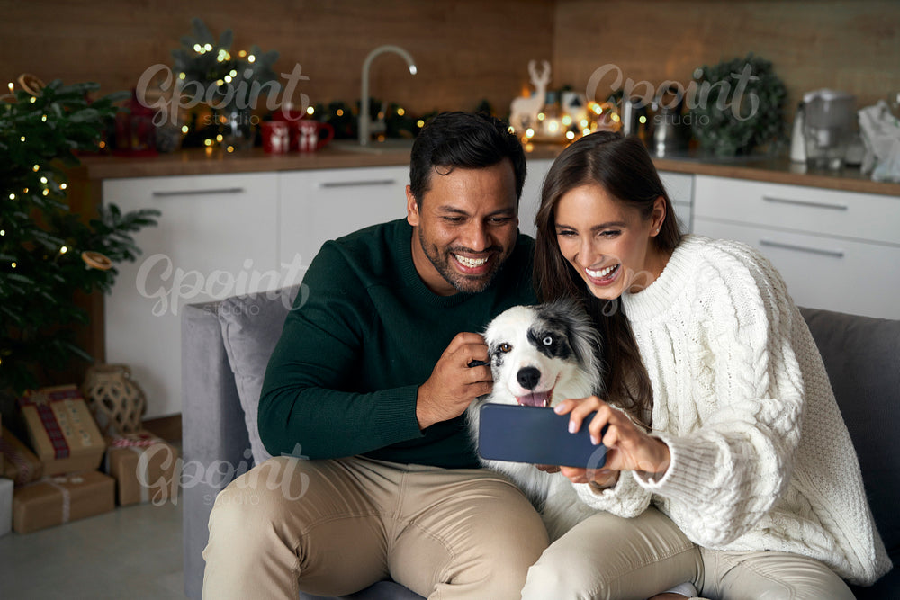 Happy multi ethnicity couple make selfie with dog at home during the Christmas 