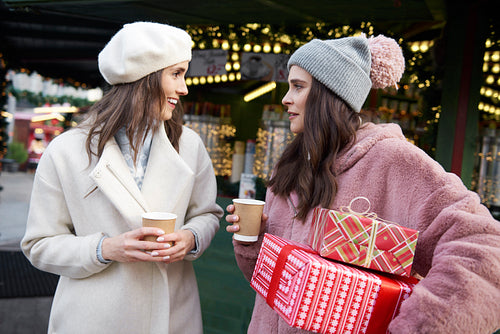 Friends on Christmas market carrying presents and drinking mulled wine