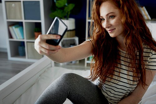 Attractive woman taking a selfie in bedroom