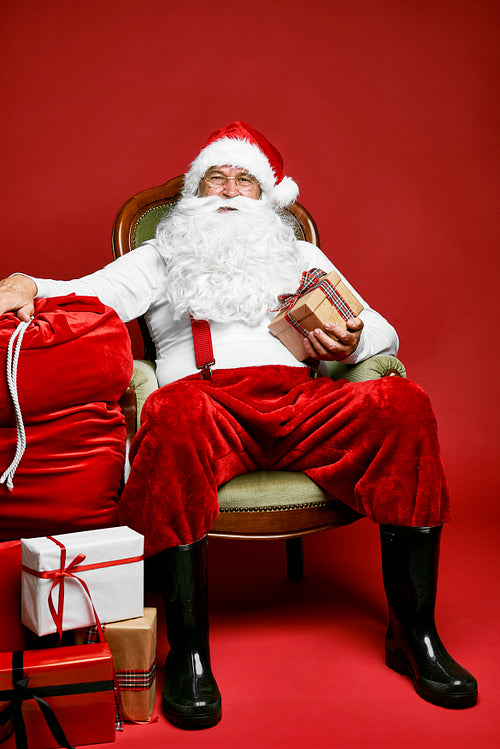 Caucasian Santa Claus sitting on the retro chair with Christmas presents