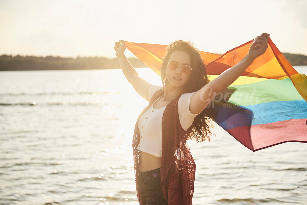 Beautiful young woman with rainbow flag at the beach