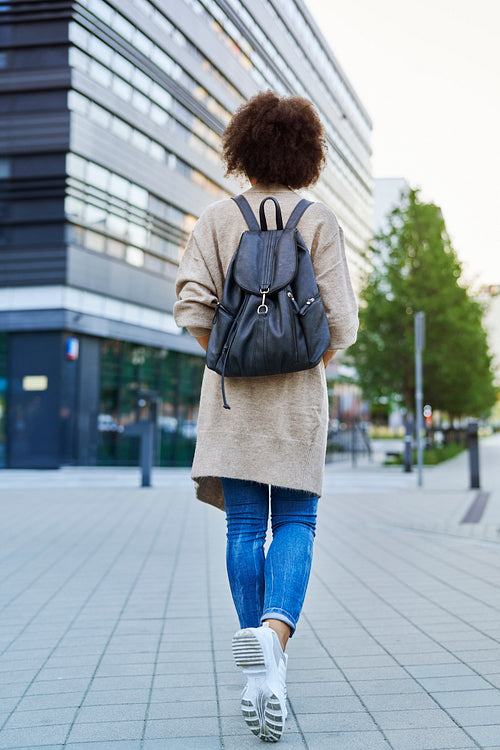 Rear view of woman walking with backpack through the city