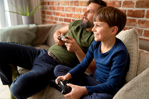 Father and son sitting at home and playing video game
