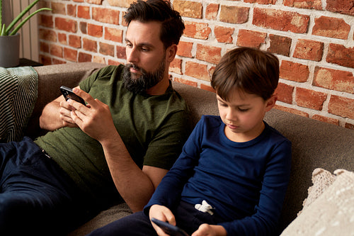 Father and son sitting with mobile phone at home