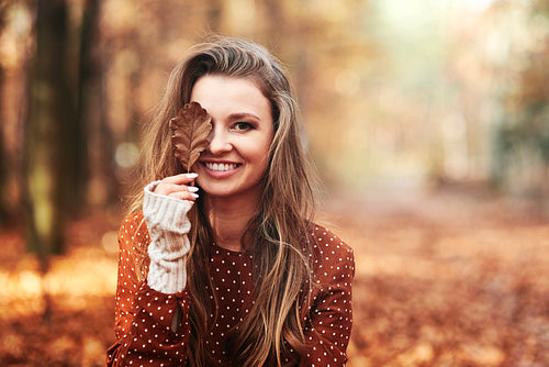 Beautiful smiling woman covering eye with autumnal leaves