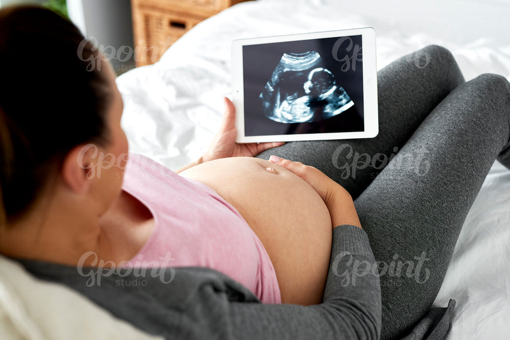 Pregnant woman watching at ultrasound record on tablet