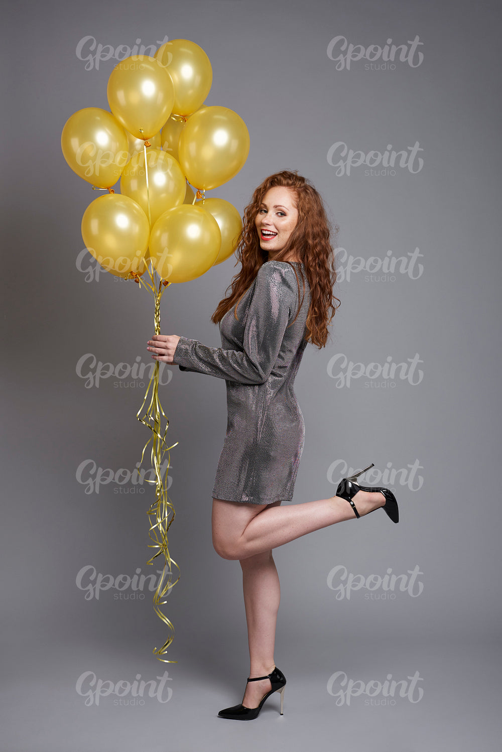 Side view of happy woman holding bunch of balloons