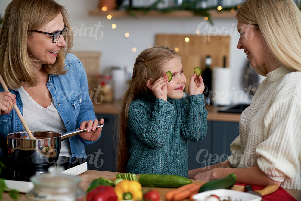 Girl playing with cucumber in the kitchen with the family