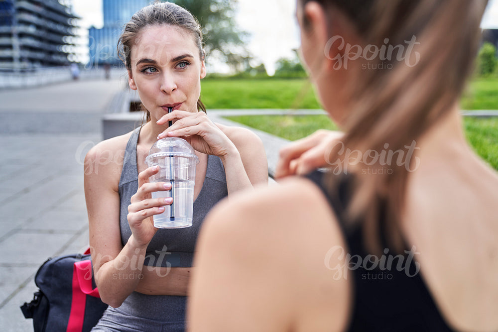 Women in training clothes sitting and drinking an isotonic drink