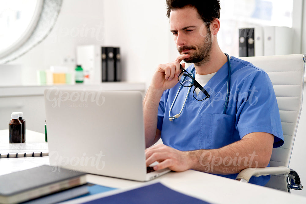 Young doctor reflects while working on the laptop