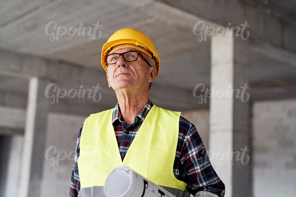 Caucasian senior engineer holding plans and looking up on construction site