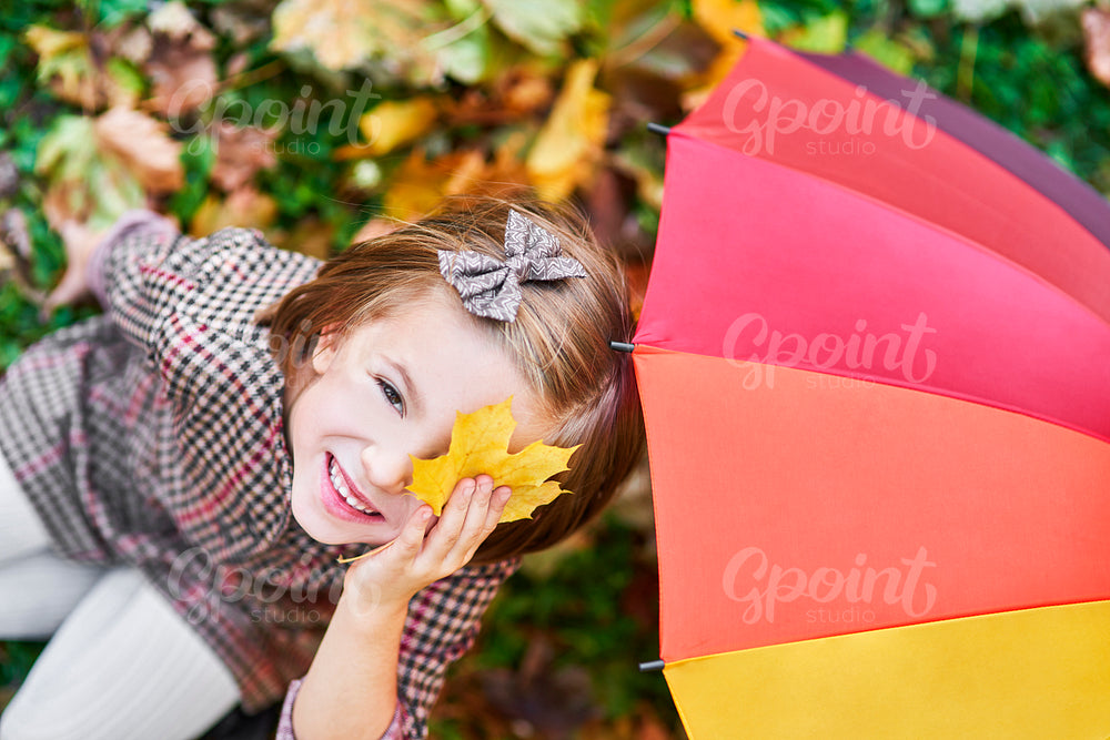 Girl having fun with autumnal leaf and colorful umbrella
